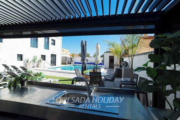A poolside area with lounge chairs, a table, and a view of a building and pool.