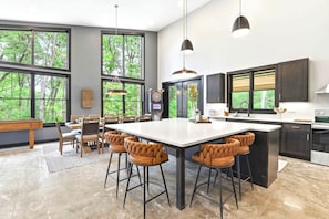 Een moderne keuken met een groot schiereiland, barstoelen en een eethoek met uitzicht op bomen.