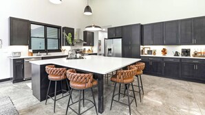 Une cuisine moderne avec des meubles de couleur sombre, un grand îlot central et des tabourets de bar.