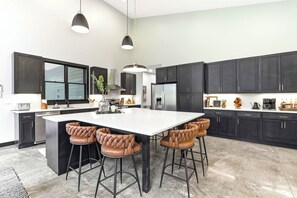 A modern kitchen with dark cabinets, a large island, and bar stools.