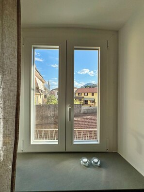 A room with a view of buildings through a window, a small table with two salt shakers, and a curtain on the left. - "C7 Balcony Railing" — New, with a balcony in Omegna (Omegna)