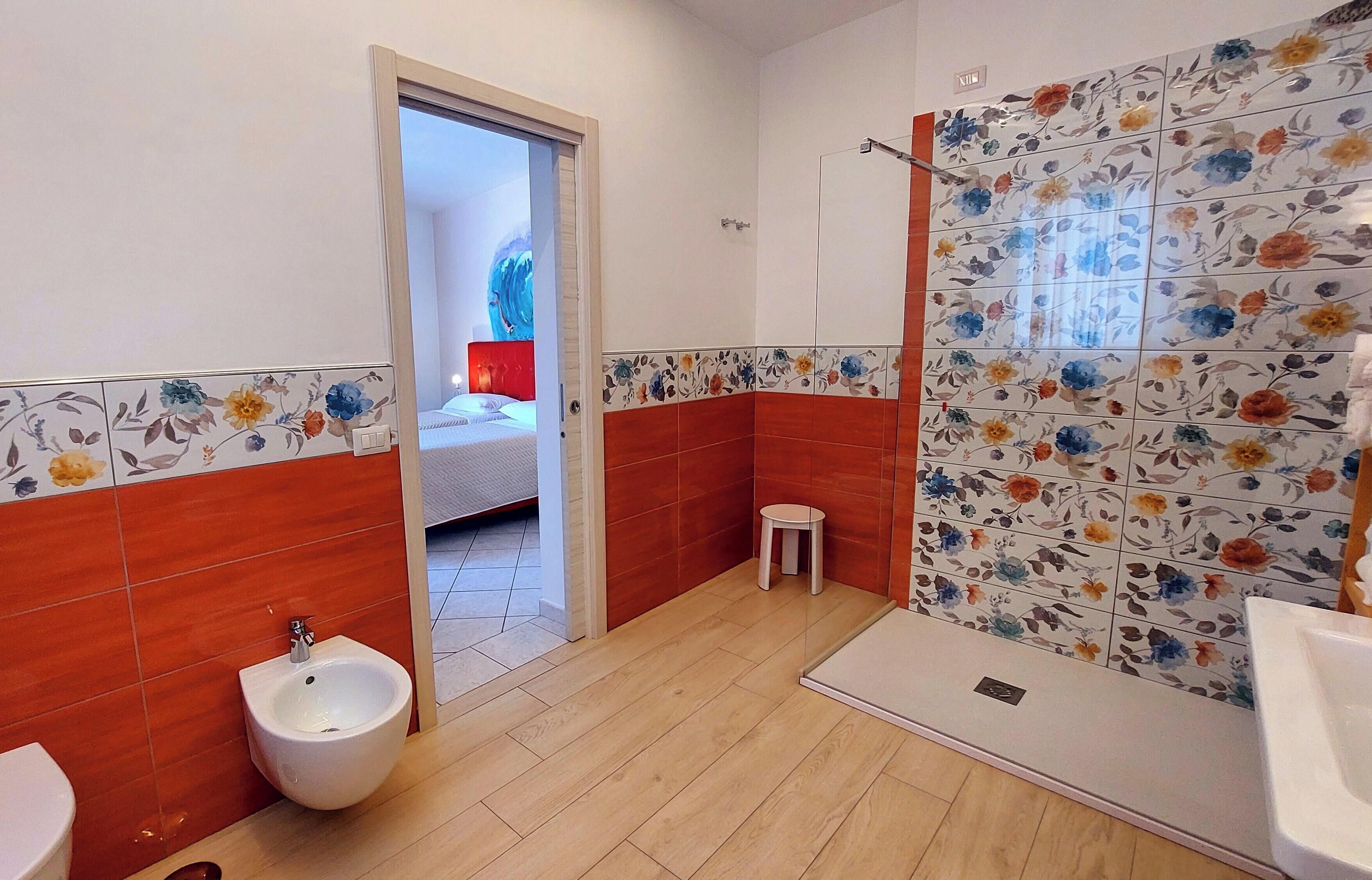 A bathroom with a bidet, toilet, shower, and a small stool.