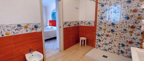A bathroom with a bidet, toilet, shower, and a small stool.