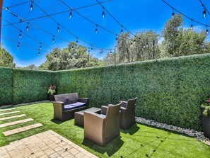 A patio area with outdoor furniture, a neatly trimmed hedge, and string lights. - The Tenley -Boutique Cottage in Tech Terrace Walk to TTU, J&B & Goodline (Lubbock)