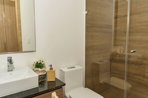 Ein Badezimmer mit weißem Waschbecken, Spiegel, Toilette und einer Duschkabine aus Glas.