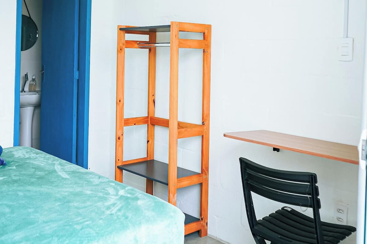 Una habitación con cama, escritorio, silla, armario y puerta al baño.