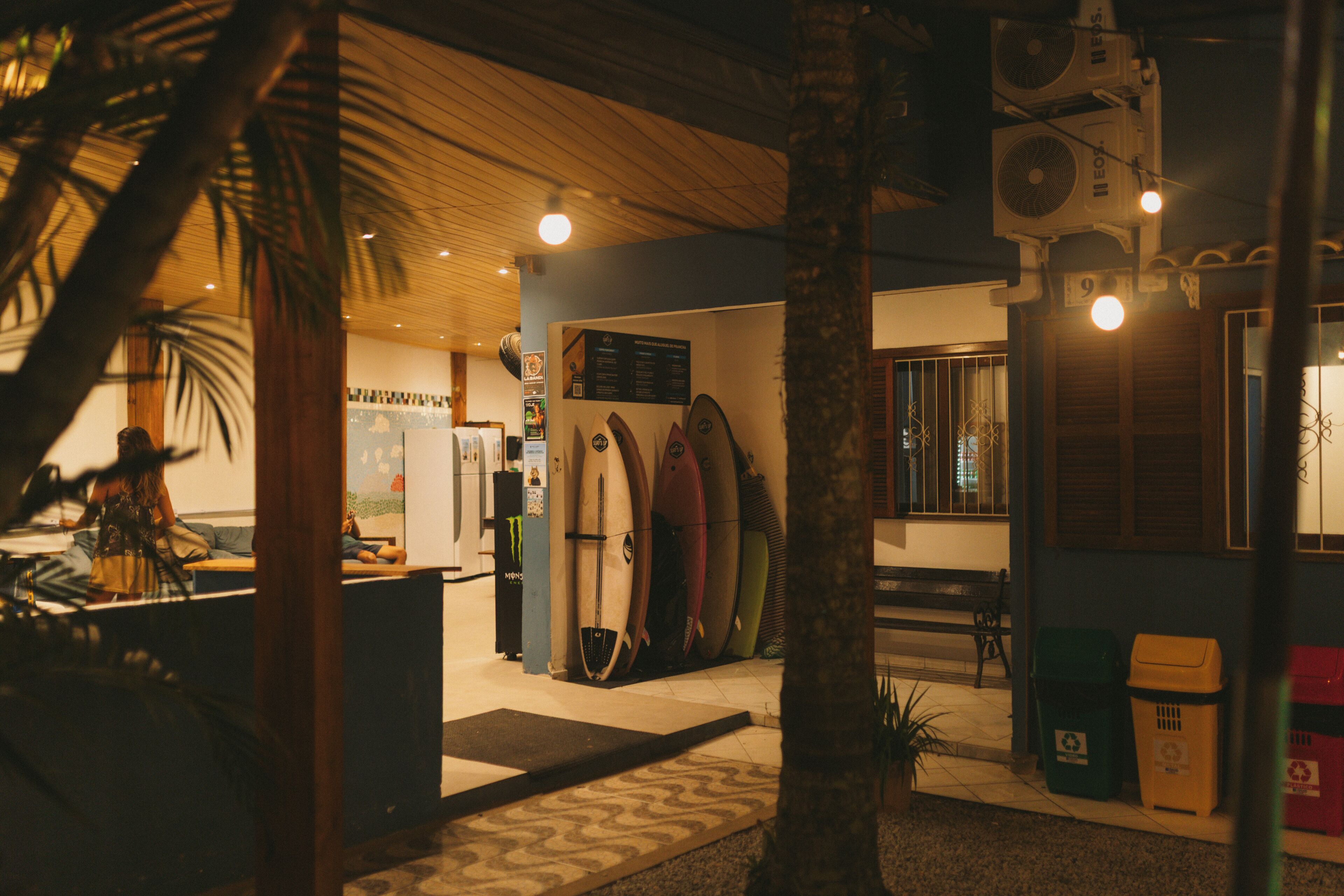 Loja de surf interior com pranchas, teto de madeira e contentores de reciclagem.