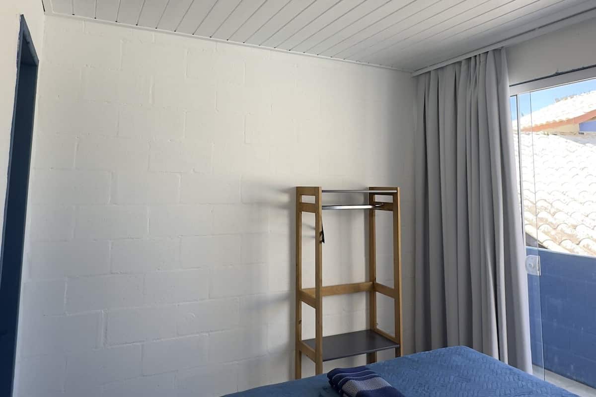 Un dormitorio con una cama, repisa de madera, ventana con cortinas y pared de ladrillo blanco.