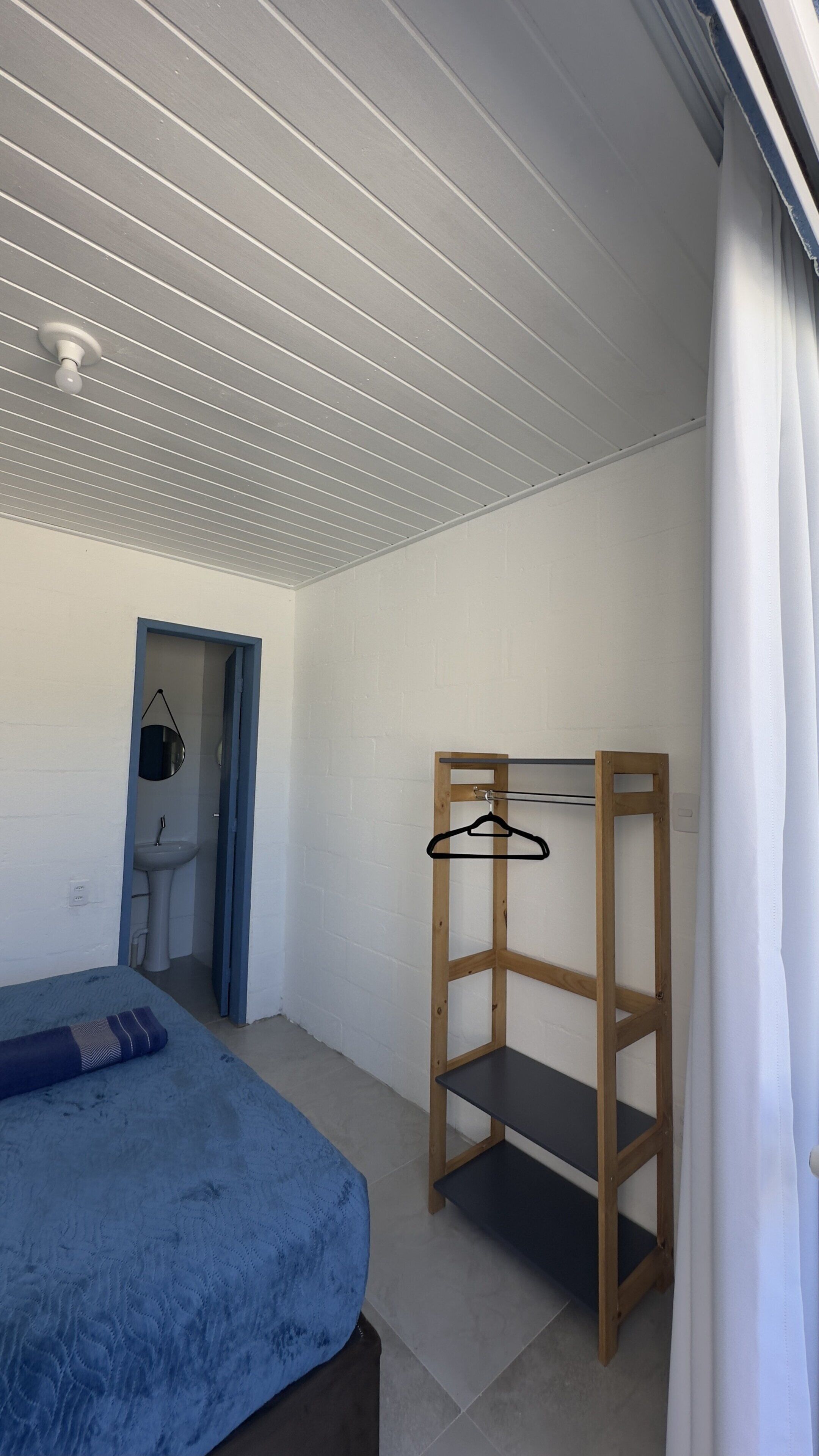 Ein Schlafzimmer mit Bett, einer Holzregaleinheit, einem Badezimmer mit Spiegel und Waschbecken sowie einer Decke mit LED-Leuchten.