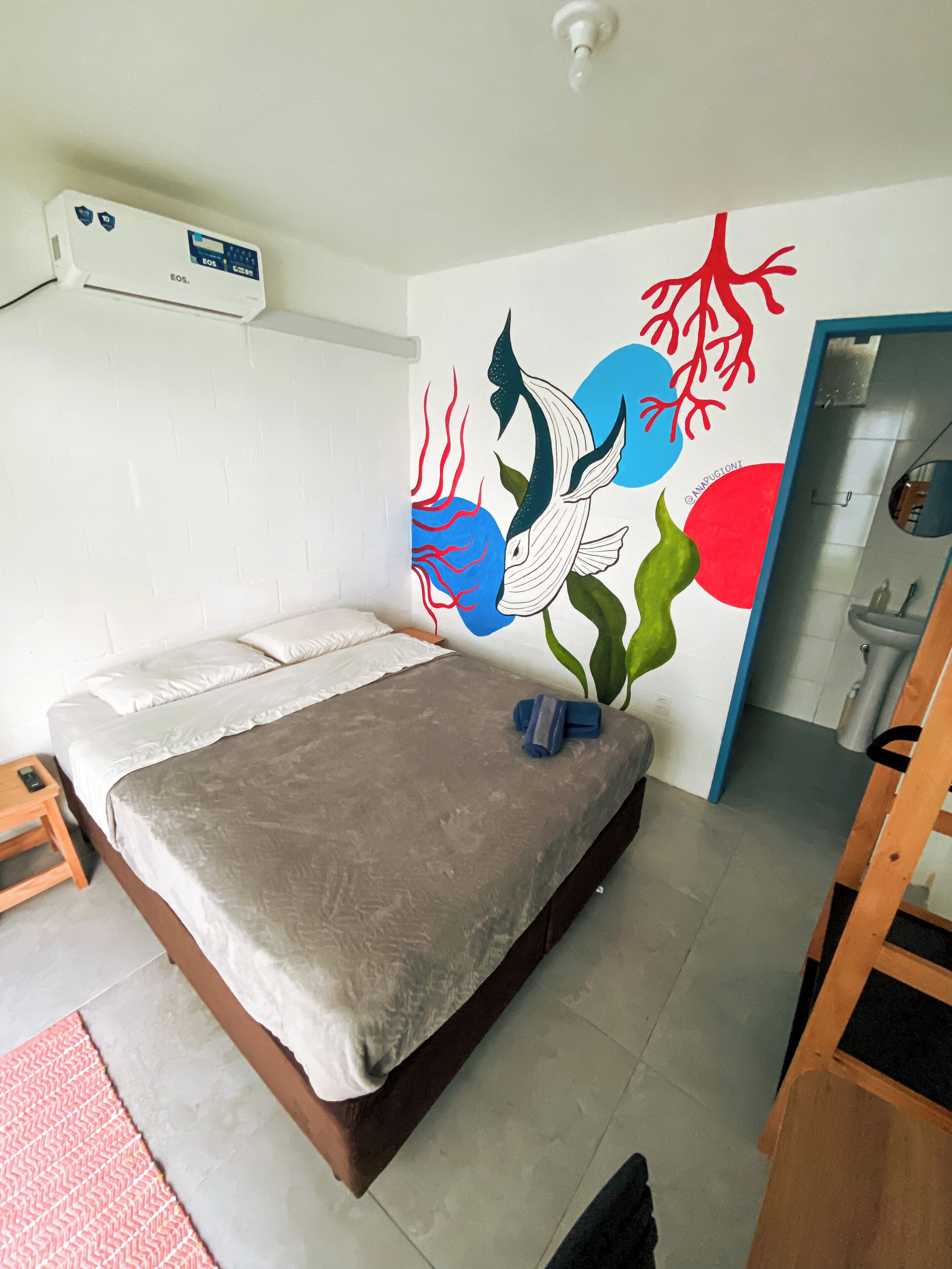 A bedroom with a bed, a wall-mounted air conditioner, and a bathroom visible through an open door.