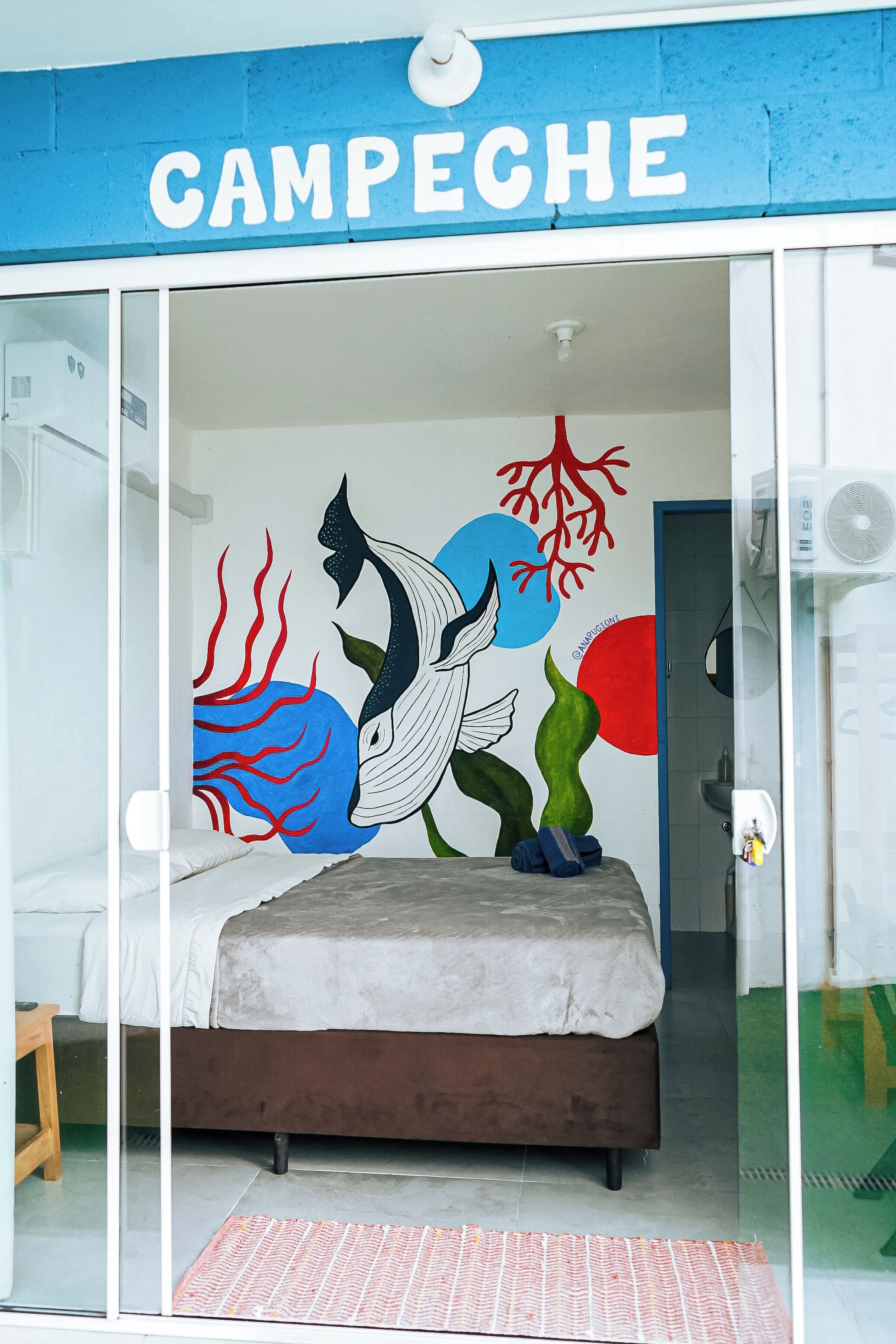 Un dormitorio con cama, un mural en la pared y un cartel azul sobre la cama.