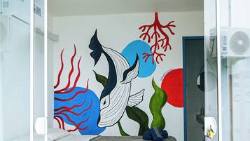 Un dormitorio con cama, un mural en la pared y un cartel azul sobre la cama.