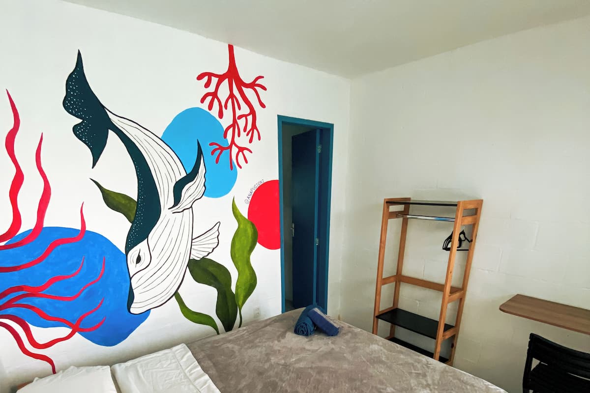 Un dormitorio con cama, un mural en la pared, un escritorio y una silla.