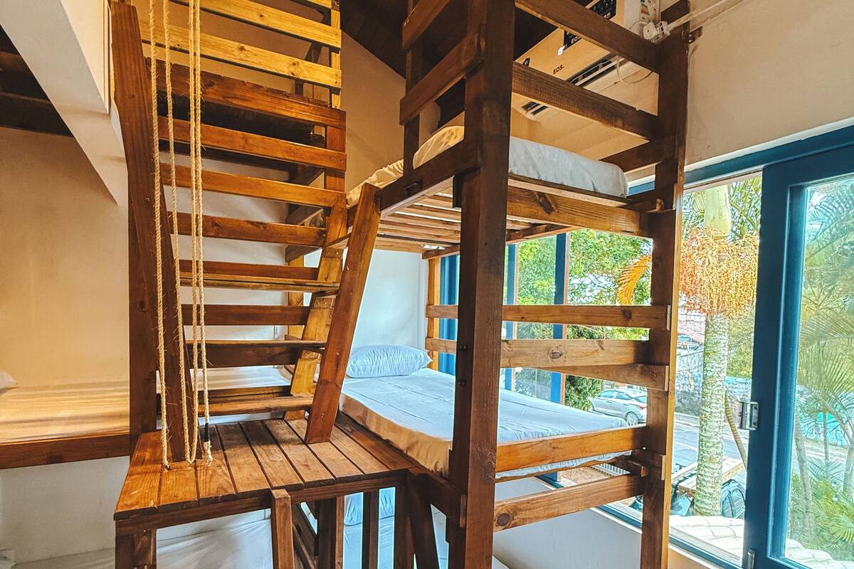 Una escalera de madera de varios niveles que conecta diferentes plantas de una habitación con un ventanal que ofrece vistas al exterior.