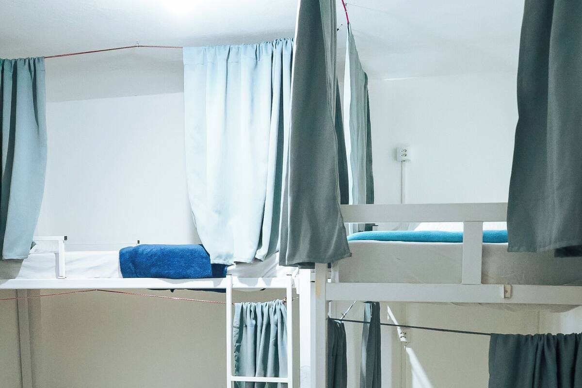 Dormitorio con literas, cortinas, pared blanca y suelo de baldosas.
