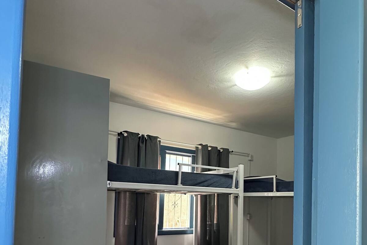 Dormitorio con literas, suelo de madera, una lámpara en el techo y una ventana con cortinas.
