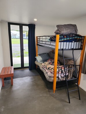 A bunk bed with a bench, a door leading outside, and a small table. - T's place Time to relax Aotea (Kawhia)