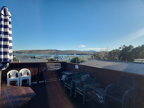 Una terraza con una parrilla, sillas y vistas a un lago y colinas.