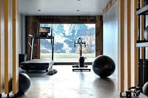 Ein Fitnessstudio mit Trainingsgeräten, Laufband und großem Fenster mit Blick auf die Berge.