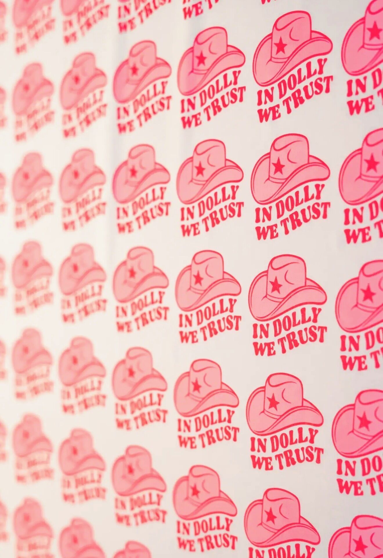 A pattern of pink cowboy hats with the text 'IN DOLLY WE TRUST' on a white background.