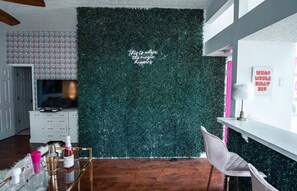 Quarto com parede verde, armário branco, televisão e uma cadeira.