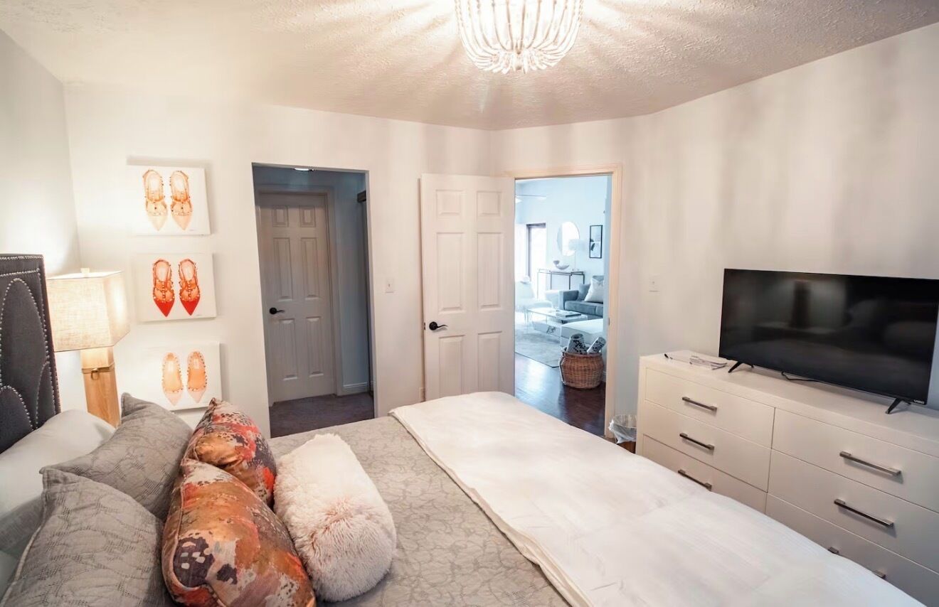 Une chambre à coucher comprenant un lit, une télévision, une commode et une porte donnant sur une autre pièce.