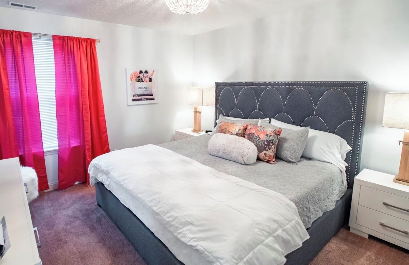 Une chambre à coucher avec un lit, des tables de chevet, une commode et une fenêtre avec des rideaux.