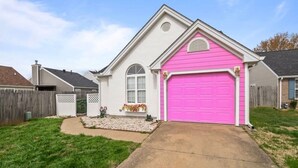 Una casa a un piano con una porta del garage rosa, una facciata anteriore bianca e un piccolo giardino con un vialetto che conduce al garage.