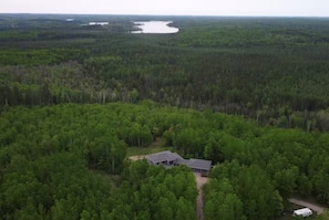 A remote cabin surrounded by dense forest with a lake in the background.