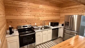 A modern kitchen with wooden walls, stainless steel appliances, and white cabinetry. - Cedar Studio w Full Kitchen + Living @ Whitetail Estates (Babbitt)