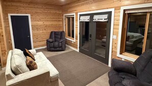 A log cabin interior with a sofa, armchair, and a door leading to another room. - Cedar Studio w Full Kitchen + Living @ Whitetail Estates (Babbitt)