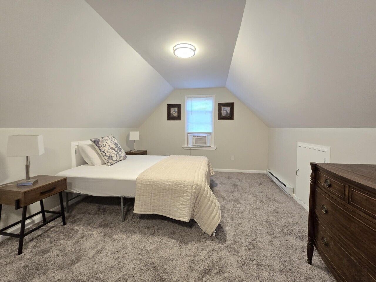 Quarto com cama, mesas de cabeceira, cômoda, janela e luminária de teto.