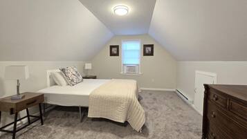 Quarto com cama, mesas de cabeceira, cômoda, janela e luminária de teto.