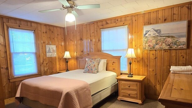 Una camera da letto con un letto, due comodini, un tavolino, una ventola a soffitto e pareti in legno.