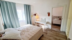 Ein Schlafzimmer mit Bett, Schreibtisch und angrenzendem Badezimmer, das durch eine offene Tür sichtbar ist.