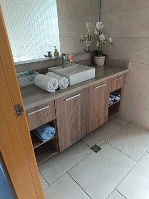 Ein Badezimmer mit Waschbecken, Spiegel, Handtüchern und einer Orchidee im Topf.