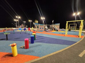Ein Spielplatz mit verschiedenen Spielgeräten, darunter Rutschen und Klettergerüsten, bei Nacht.