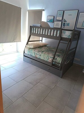 Ein Etagenbett mit unterem Bett, ein Fenster mit Jalousie und gerahmte Bilder an der Wand.