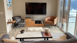 Een moderne woonkamer met een grote flatscreen televisie, een bank, een salontafel en uitzicht op de zee door grote ramen.