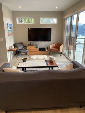 Ein modernes Wohnzimmer mit einem großen Flachbildfernseher, einer Couch, einem Couchtisch und Meerblick durch große Fenster.