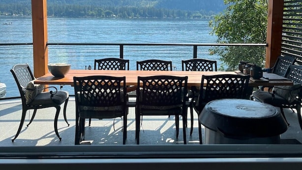 Een overdekt terras met een tafel en stoelen, met uitzicht op een meer en bergen op de achtergrond.
