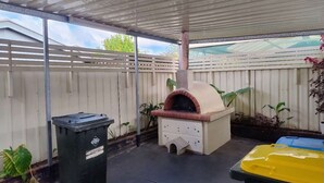 Katettu ulkoalue, jossa on tiilistä rakennettu pizzauuni, roskakori ja keltainen säiliö.