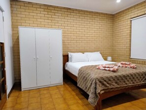 Ein Schlafzimmer mit Backsteinwand, einem Bett mit weißer Bettwäsche, einer braunen Decke und einem weißen Kleiderschrank.