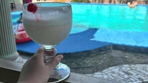 Una mano sosteniendo un vaso con una cereza, con vista a una piscina.