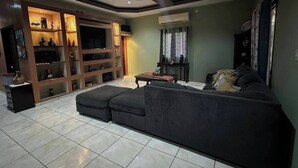 Una sala de estar con un sofá modular, un televisor y una estantería con objetos decorativos.