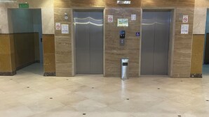 An elevator area with two elevators, a trash bin, and a sign indicating a stairwell. - Rimas Al Anoud Hotel (Makkah)