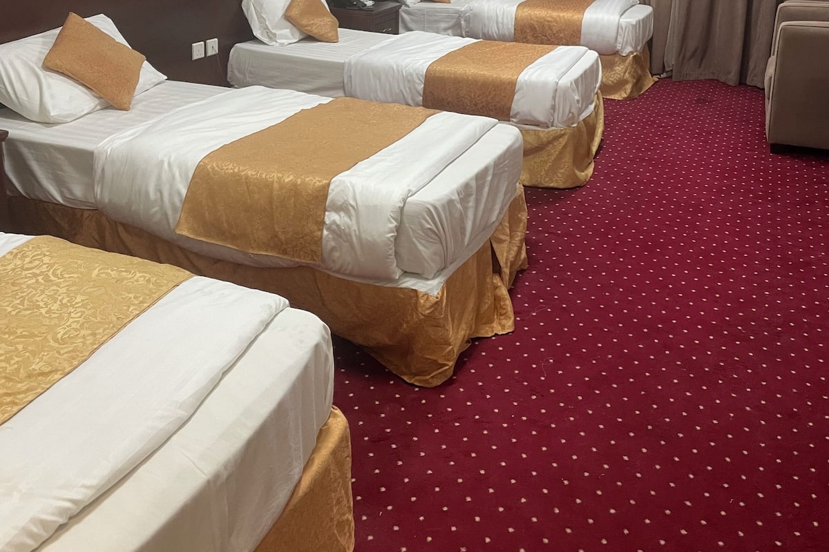 Habitació d'hotel amb tres llits individuals, una catifa vermella i una làmpada al sostre.