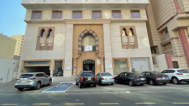 A multi-story building with a central entrance, parking lot, and several parked cars. - Rimas Al Anoud Hotel (Makkah)