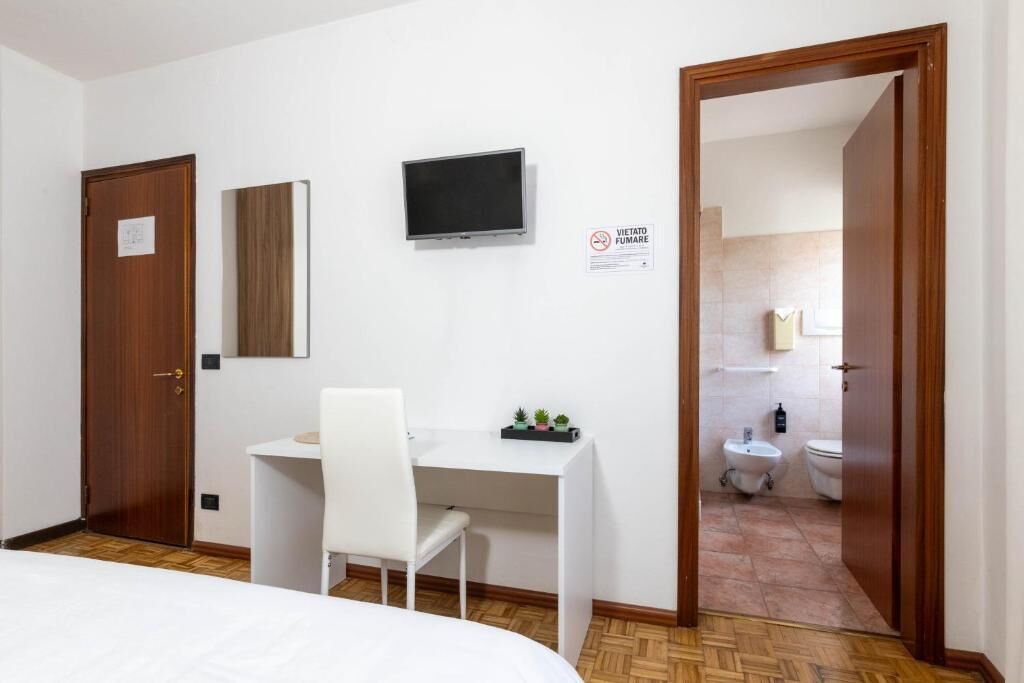 A hotel room with a bed, a desk with a chair, a television, a door, and a bathroom visible through an open door.