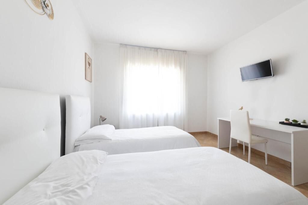 A hotel room with two beds, a desk, a chair, a TV, and a window with curtains.